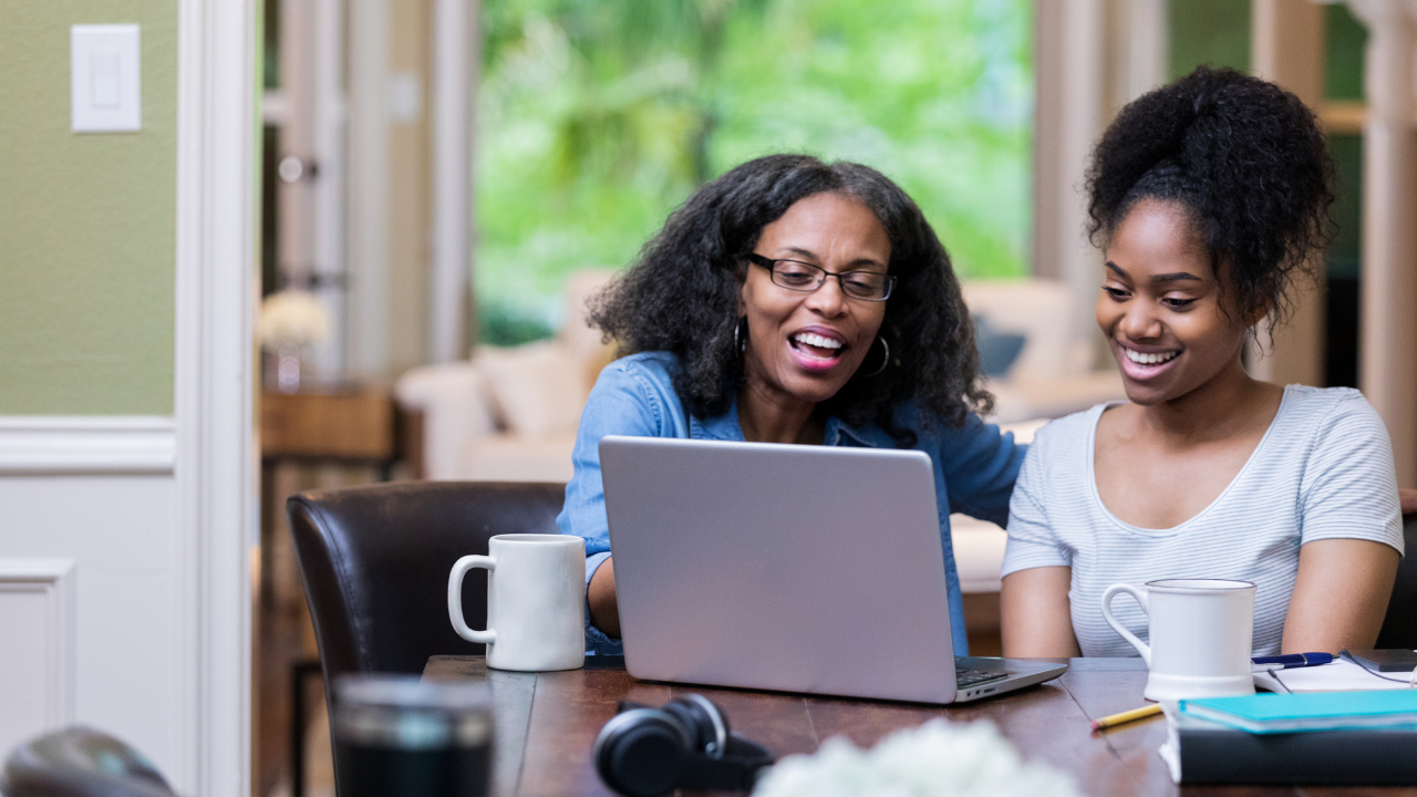 Mom and daughter sitting at table looking at laptop